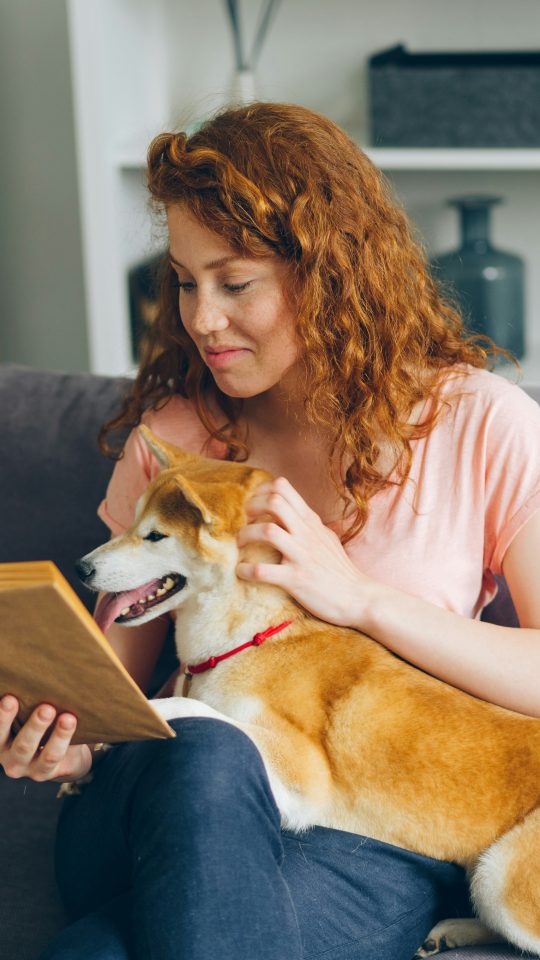 a woman sitting on a couch with a dog reading a book